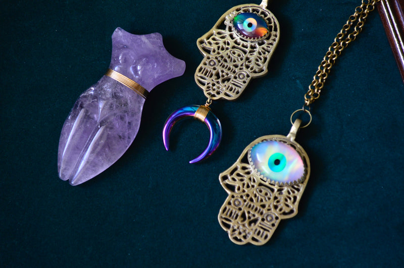 Several Hand with Eye in the middle jewelry pieces against a dark background.