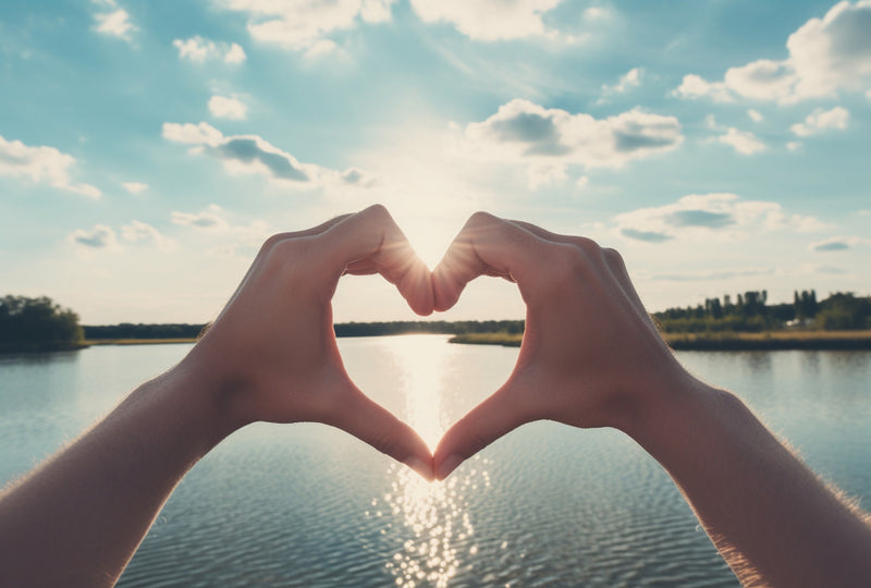Two hands make the heart symbol with water in the background.