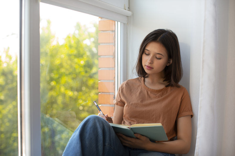 Young woman writing in a journal by the window.