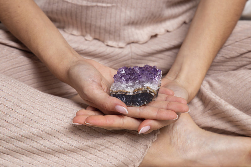 Woman holding an amethyst crystal in the palm of her hand.