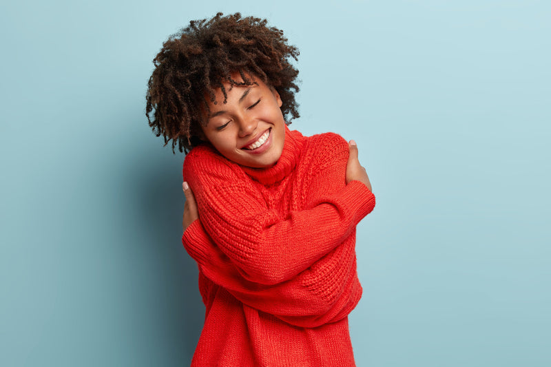 Model wearing a red sweater wraps her arms around herself in an act of self-love.
