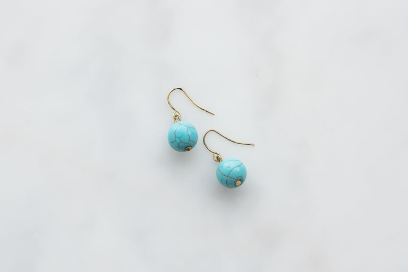 Turquoise blue hoo earrings against a blue background.