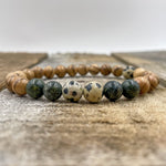 Another view of the gemstones Dalmatian, Serpentine, & Sandalwood on a wooden surface.