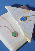 The Hamsa Green Opalite and Blue Turquoise Necklaces are displayed together against a marble surface.